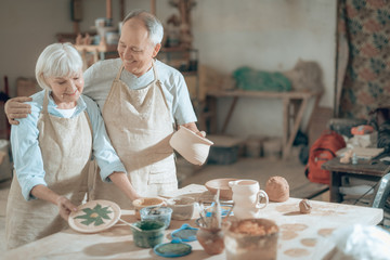 Half length of happy mature potters posing for camera in workshop