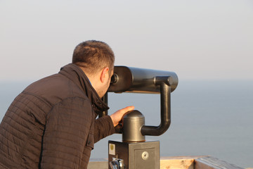 man examines the landscape in the binocular during sunset at sea