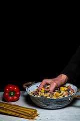 hand grabs conchiglie pasta out of white vintage bowl. Black backgroud, copy space