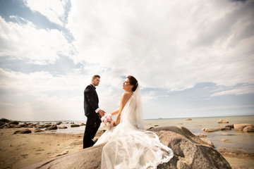 Stylish wedding couple standing on sea shore. Newlyweds are walking by the sea