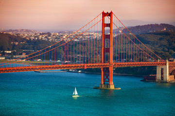 Yacht, die bei Sonnenuntergang unter der Golden Gate Bridge vorbeifährt