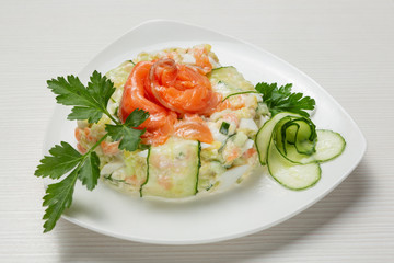 salad of boiled vegetables, with salmon, decorated with greens and slices of fresh cucumber, on a white plate