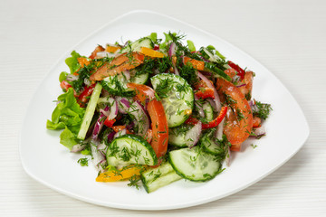 rustic salad of fresh cucumbers, tomatoes and onions, decorated with greens, on plate