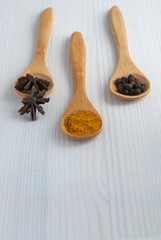 Vertical close-up of three wooden spoons with spices. Starry anis, curry and black pepper on white wooden background with copy space