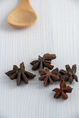 Vertical close-up of star anise with wooden spoon on white mader background with copy space