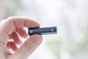 battery cell in hand at light abstract background.