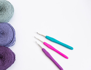 Multi-colored balls of wool for crocheting and needlework and crochet hooks on a white background
