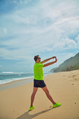 Sportsman stretching on a tropical sandy beach.