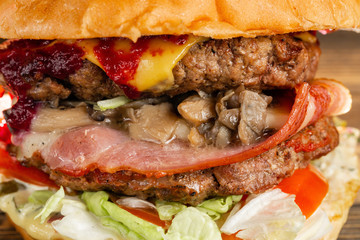 A big burger with two beef cutlets, cooked on charcoal. Lunch on a wooden background. The concept of fast food and not healthy food