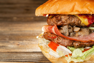A big burger with two beef cutlets, cooked on charcoal. Lunch on a wooden background. The concept of fast food and not healthy food