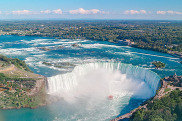 Aerial top landscape view of Niagara Falls  between United States of America and Canada. Horseshoe of Canadian waterfall on sunny day. Water tour boat at famous tourist landmark - obrazy, fototapety, plakaty