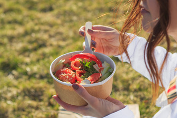 Smiling hipster woman having a relaxing lunch break outdoors, she is sitting on the grass and...