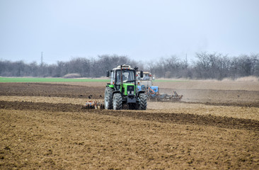 Obraz premium Lush and loosen the soil on the field before sowing. The tractor plows a field with a plow