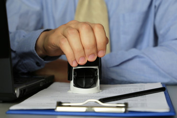 Fototapeta premium Man in business clothes puts a stamp on the documents in the office. Concept of official, custom officer, manager, permission, businessman, contract