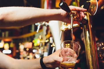 We meet oktoberfest. Hand of bartender pouring a large lager beer in tap. Pouring beer for client. Side view of young bartender pouring beer while standing at the bar counter.
