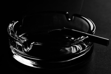 Cigarette and glass ashtray on black background with copy space