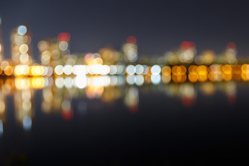 blurred dark cityscape with illuminated buildings, reflection and bokeh lights