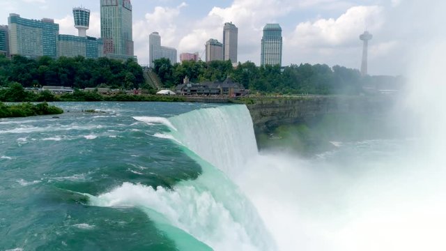 NIAGARA FALLS, US-CANADA BORDER. 4K Drone slow motion shot of the residential area behind the waterfall. Powerful giant flow of water - side view
