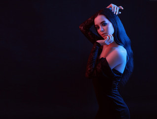 Neon light. Portrait of sexy elegant  beautiful brunette young woman in evening fashionable stylish black dress. Model with trendy evening smoky eyes makeup touching her face. Dark background.