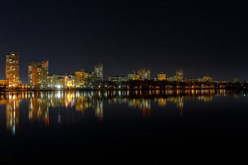 picturesque dark cityscape with illuminated buildings, river and night sky
