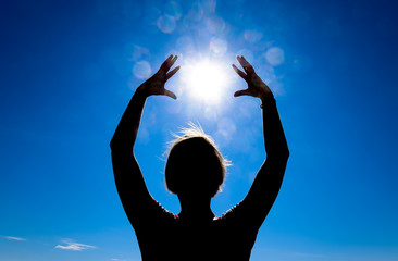 Silhouette of a girl against the background of the sun and blue sky. Hands are raised up to the sun