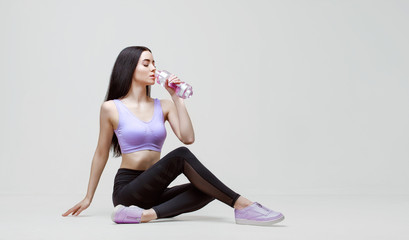 Amazing woman in trendy sportswear drinking water from bottle to stay hydrated after workout....