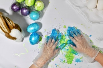 Children's hands in colored gloves leave blue prints on the surface after painting Easter eggs.