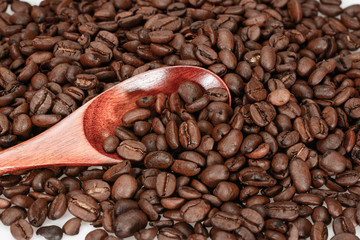 Hard roasted coffee beans, dark brown with bamboo spoon close up isolated on a white background