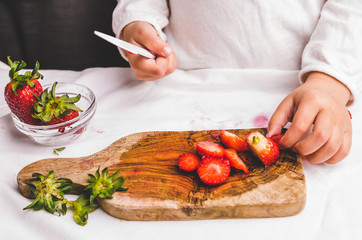 Mother helps child to slice strawberry with knife