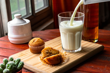 milk falling into a glass cup on a wooden board, accompanied by muffins and honey