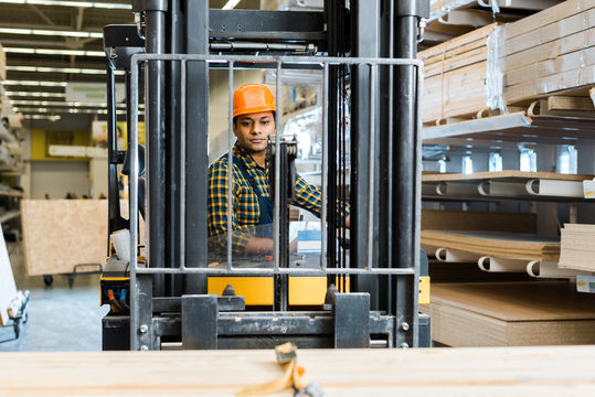 selective focus of handsome, conentrated indian worker sitting in forklift machine in warehouse