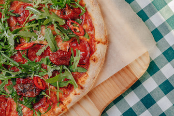 Neapolitan spicy pizza with ham, cheese, arugula, basil, tomatoes, pepperoni pepper sprayed with cheese on a wooden board on a tablecloth in a cell with a place for text