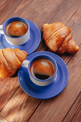 two cups of coffee and croissants on a wooden background, good light, morning atmosphere