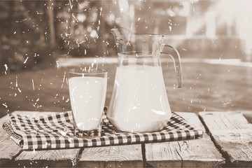 A glass of milk and a milk jug on plaid tablecloth