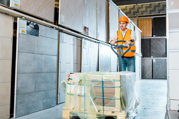 smiling warehouse worker carrying pallet jack in tiles department