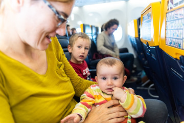 Baby entertaining in the arms of his mother sitting in the seat of an airplane during a long trip.