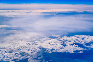 Intense blue sky with white clouds and plane crossing it, seen from above in another plane.