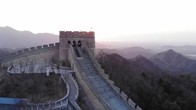 Reconstructed watch tower at Great Wall of China, aerial shot at evening time. Unidentified people look around building. Camera fly back, sun light shine from behind fortification