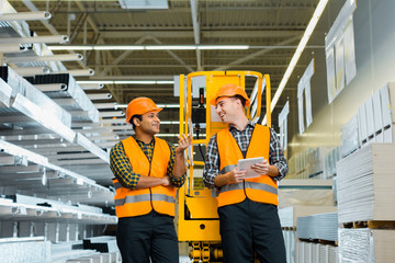 Fototapeta na wymiar selective focus of cheerful multicultural workers talking while standing near scissor lift