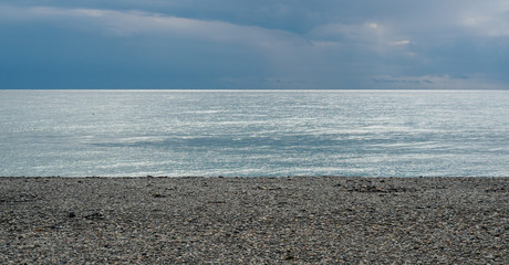 A strip of blue sky and sea over the pebbly shore