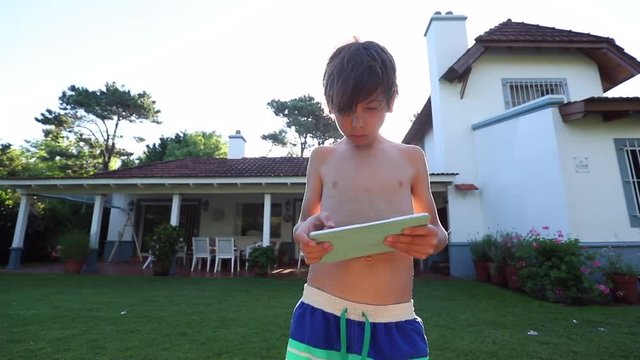 Child boy holding tablet device outside in front of house