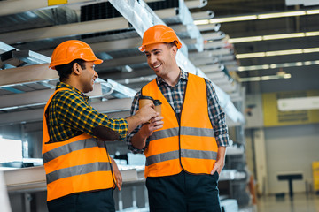 selective focus of multicultural workers clinking with paper cups in warehouse