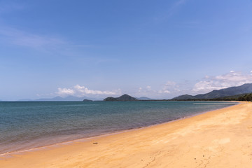 Cairns, Australia - February 18, 2019: Warm beige tropical beach of Palm Cove with azure Coral Sea water under blue sky with rainforested mountains on horizon.