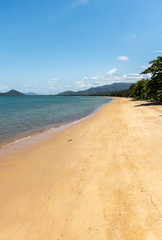 Cairns, Australia - February 18, 2019: Warm beige tropical beach of Palm Cove with azure Coral Sea water under blue sky with rainforested mountains on horizon.