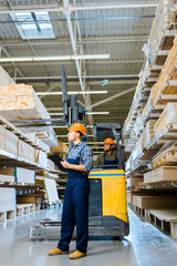 serious worker with clipboard standing near indian colleague in forklift machine