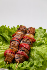 Pieces of fried meat and vegetables on skewers lying on a plate on a sheet of salad on a white background.