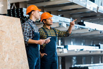 attentive indian warehouse worker pointing with hand near handsome colleague