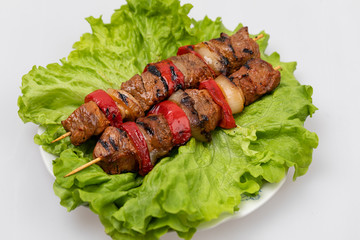 Pieces of fried meat and vegetables on skewers lying on a plate on a sheet of salad on a white...