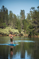 A an active boy paddling a paddle board on Whiskeytown Reservoir in the Sierra Nevada Mountains of Northern California on a warm summer day.