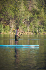 A boy paddling a paddle board on Whiskeytown Reservoir in Northern California on a warm summer day.